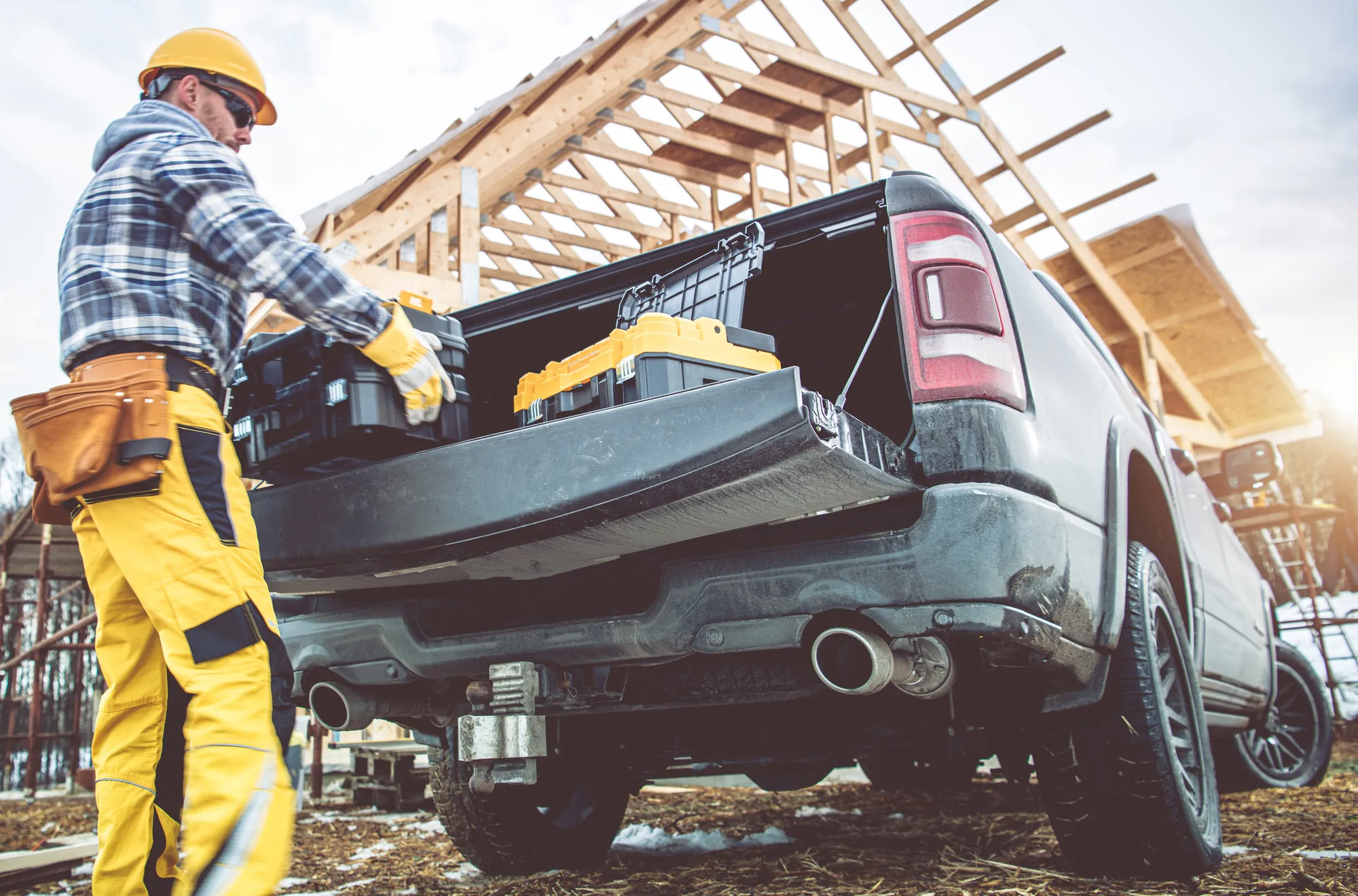 Contractor loading toolboxes into the bed of a pickup truck at a house framing site